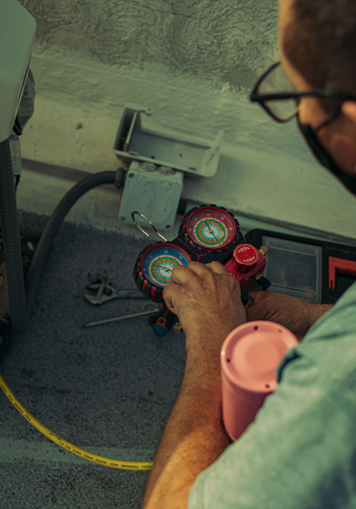 A technician reading a refrigerant manifold gauge set next to an air conditioning unit